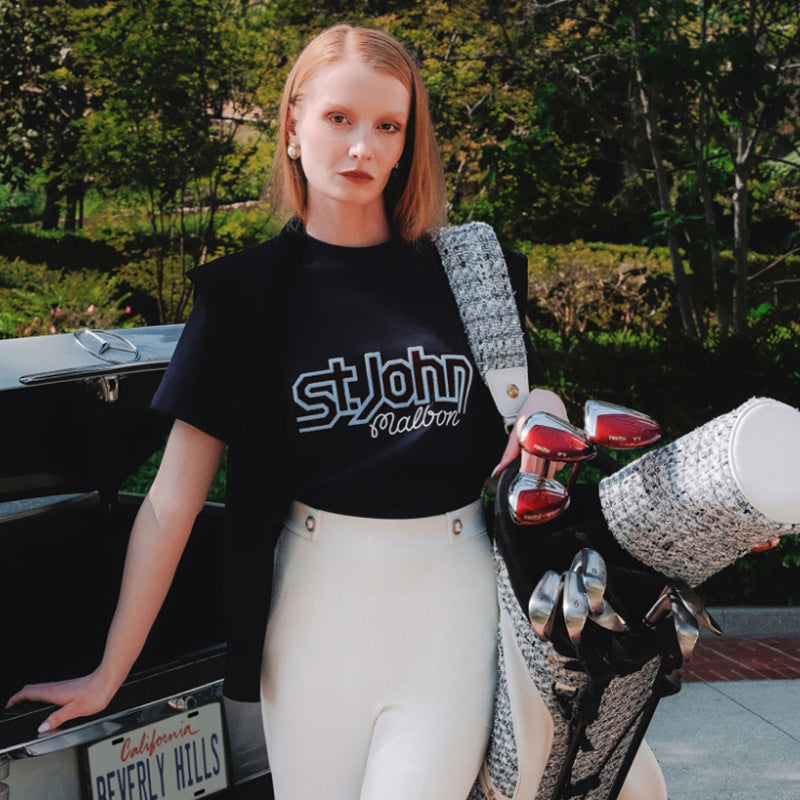 Woman wearing a black St John Knits Malbon t-shirt with 'St. John' logo next to a car with a shiny exterior.