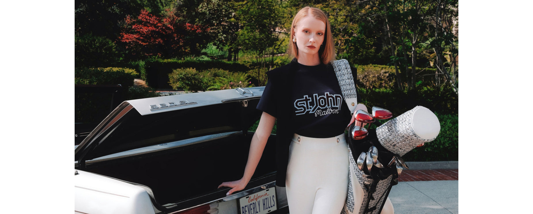 Woman wearing a black St John Knits Malbon t-shirt with 'St. John' logo next to a car with a shiny exterior.